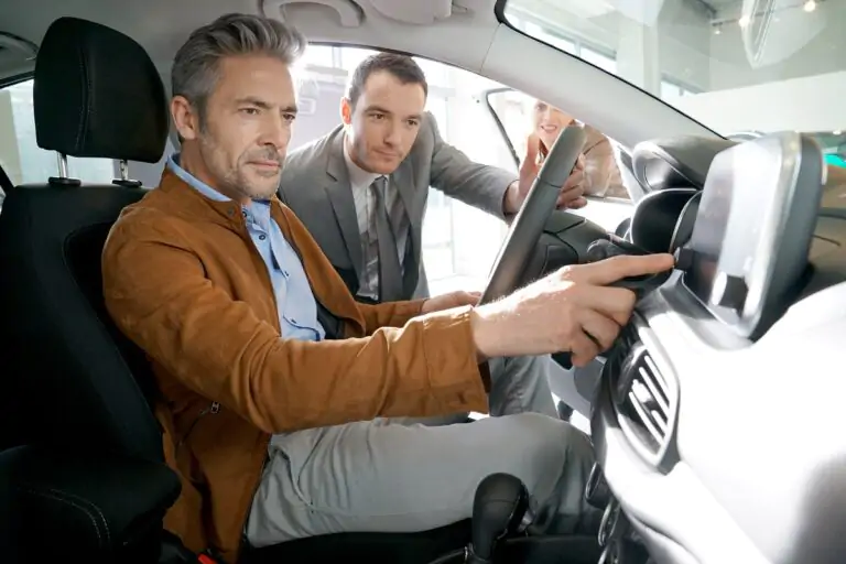 2 men looking at a car's navigation system, the man is touching the screen, the woman is pointing at it, the car is parked in a showroom.