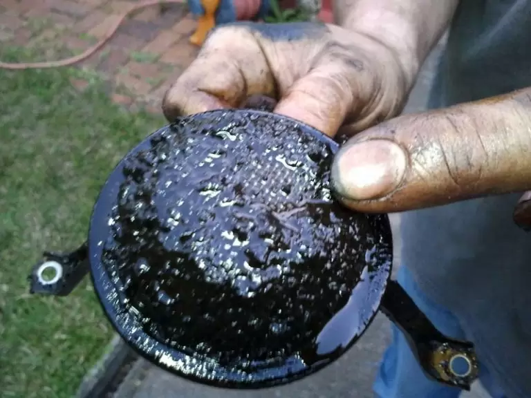 A dirty oil filter from a car engine, held by a dirty hand, close-up, industrial, dirty, grimy 