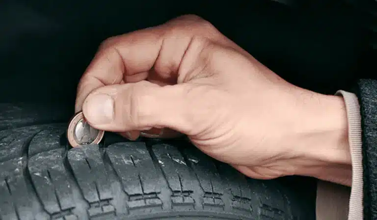 In a well-lit space, a person examines a tire closely, using a penny to check the tread depth. Explore the importance of regular tire maintenance and the role it plays in ensuring safety on the road.