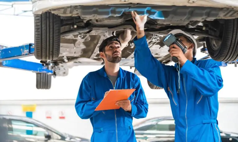 Two mechanics in blue overalls collaborate under the hood of a parked car, one holding a wrench while the other examines a paper. Explore the teamwork and expertise required to troubleshoot and resolve common mechanical issues, ensuring the smooth operation of vehicles.