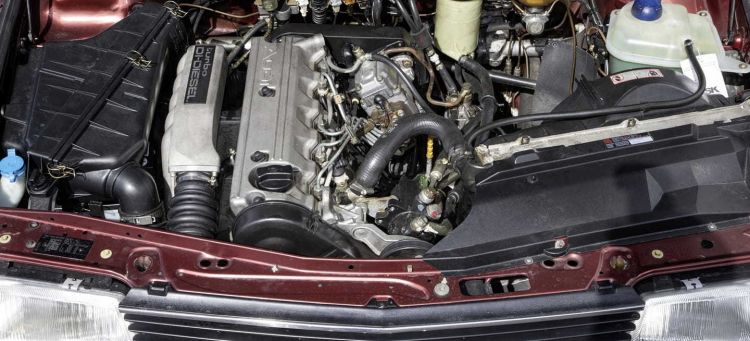 A close-up of the engine bay of an Audi 100 2.5 Tdi. The engine is a 5-cylinder, 2.2-liter inline-5 with a turbocharger and intercooler. The engine is paired with a 5-speed manual transmission and quattro all-wheel drive. The car is finished in red with a black interior.