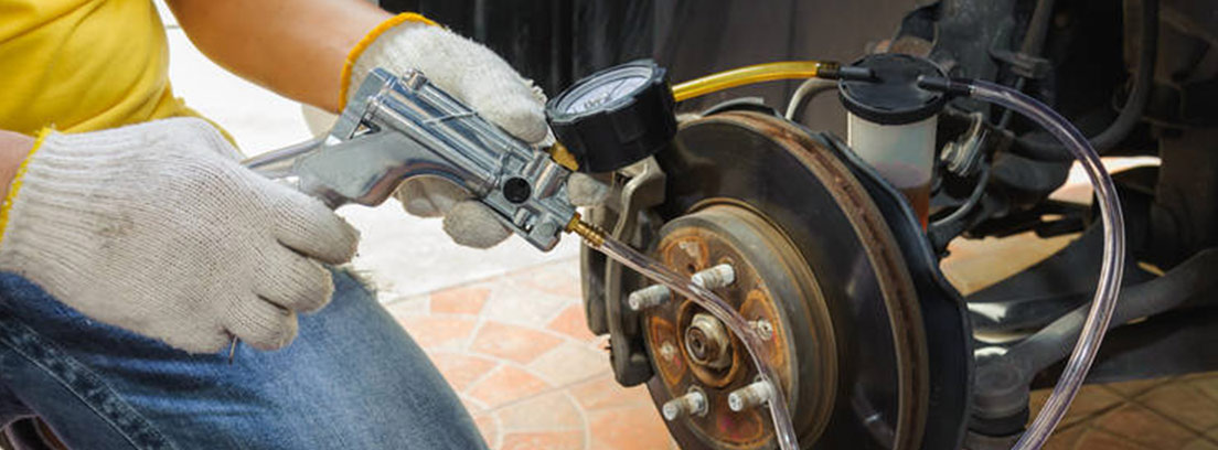 Person kneeling next to car wheel with tube connected to the bleeder.